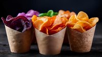 Colorful vegetable chips served in brown paper cones on dark background, healthy snack alternative featuring beet, sweet potato and carrot crisps.