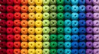 Colorful rainbow gradient yarn balls arranged in organized rows creating vibrant spectrum pattern for crafting and textile projects.