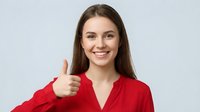 Young professional woman with long brown hair giving thumbs up gesture in red business shirt, smiling confidently at camera on white background.