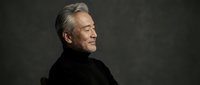 Senior Caucasian man with gray hair in black turtleneck against dark background, profile portrait showing contemplative expression for professional headshots.