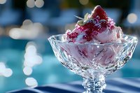 Creamy vanilla ice cream topped with fresh strawberry in elegant crystal dessert bowl against sparkling bokeh background, soft focus food photography.