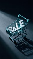 Mini teal shopping cart with white sale letters on dark background, dramatic shadow, retail discount and e-commerce promotion concept.