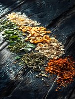 Colorful array of dried herbs, spices, and sliced mushrooms arranged in diagonal lines on dark rustic wooden surface with dramatic side lighting.