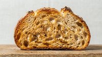 Sliced artisan sourdough bread with open crumb structure displayed on wooden surface, suitable for bakery, food, and culinary content.