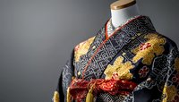 Traditional Japanese kimono with geometric pattern in black and gold, decorated with ornate obi sash, displayed on mannequin against dark background.