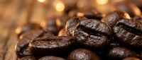 Roasted coffee beans closeup on rustic wooden surface with warm golden bokeh lights, rich dark brown tones evoking aroma and freshness.