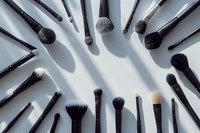 Professional makeup brushes arranged in circular pattern casting dramatic shadows on light background, beauty industry concept for cosmetics application.