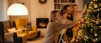 Multigenerational family decorating illuminated Christmas tree together in warm living room with fireplace and holiday lights during festive season celebration.