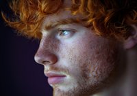 Young redhead man with freckles and curly hair in dramatic lighting. Portrait photography for fashion, beauty campaigns and lifestyle projects.
