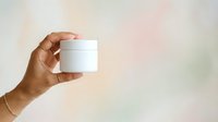 Male hand holding white cosmetic jar against soft blurred background, suitable for skincare, beauty product packaging, and wellness branding applications.