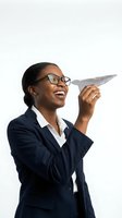 Happy African American businesswoman in navy suit holding paper airplane on white background for business and career concepts.