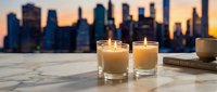 Two glowing candles on marble surface with blurred city skyline at sunset creating warm ambiance for relaxation, meditation, and home decor concepts.