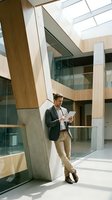 Professional businessman using tablet in modern office building atrium with natural light and contemporary architecture for corporate communication.