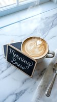 Steaming latte with leaf art on marble surface beside a Morning Brew chalkboard sign, spoon and linen napkin in soft natural light.