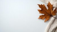 Brown dried maple leaf on cozy knitted beige sweater texture against white background, creating minimalist autumn composition with copy space.
