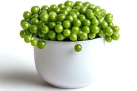 Fresh green peas overflowing from white ceramic bowl on white background, minimalist food composition for healthy eating and cooking concepts.