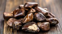 Fresh raw cacao beans scattered on rustic wooden table, showing natural chocolate texture and rich brown colors in macro photography.
