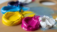 Colorful acrylic paint swirls in blue, yellow, magenta and white on artist palette with brushes for creative artwork and painting projects.