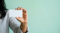 Close-up of a person's hand holding a blank white card against a mint green background, suitable for business cards, marketing materials, and promotional designs.