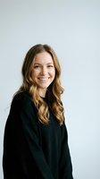 Young Caucasian businesswoman with blonde wavy hair smiling confidently in black sweater against white background for professional headshots.