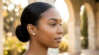 Young African American woman with elegant low bun hairstyle and pearl earrings in warm golden hour lighting for beauty and lifestyle content.