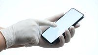 Caucasian male hand wearing white latex glove holding smartphone with blank white screen, isolated on white background for healthcare, medical, technology, and design mockup applications.