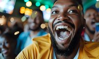 Young African American man laughing with genuine joy and excitement at sports bar, wearing yellow t-shirt, with blurred crowd and bokeh lights in background.
