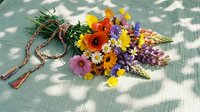 Colorful wildflower bouquet with rope binding on green checkered fabric, featuring daisies, poppies and mixed blooms for rustic country decor and crafts.
