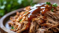 Tender pulled pork with sweet and smoky barbecue sauce garnished with fresh herbs on rustic wooden plate, macro food photography with selective focus.