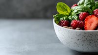 Fresh raspberries and strawberry in speckled ceramic bowl with green basil leaves on gray background, healthy breakfast concept with copy space for text.