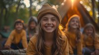 Young woman in yellow sweater and beanie smiling brightly at sunset with friends in background, capturing genuine joy and friendship in outdoor setting.