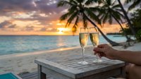 Champagne glasses on tropical beach table at sunset with palm trees and ocean view for romantic vacation celebration and luxury travel moments.