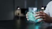 Hands of a male professional with medium skin tone holding a glowing turquoise digital sphere with particle effects, representing technology, innovation, and data management in a modern office setting.