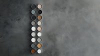 Minimalist arrangement of round ceramic buttons in white, gray and brown tones on textured concrete background, forming vertical pattern for modern interior design.