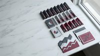 Handmade accordion fold books and greeting cards in burgundy and gray tones arranged on a marble surface near a window.