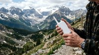 Hiker holding blank white smartphone with mountain valley landscape in background, outdoor adventure and mobile technology concept for travel and hiking applications.
