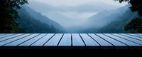 Panoramic view from wooden deck overlooking misty mountain valley at dawn, empty rustic platform against foggy blue hills and forest landscape.