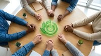 Business team collaboration around green recycling symbol on wooden table representing environmental sustainability and corporate responsibility in office.