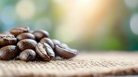 Freshly roasted coffee beans scattered on burlap fabric with soft bokeh background, macro close-up view showing rich brown texture and natural lighting.