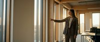 Professional businesswoman in suit pointing forward in modern office with large windows during golden hour lighting for corporate presentations.