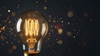 Vintage Edison light bulb with glowing filament against dark background with golden bokeh lights creating warm atmospheric lighting for creative projects.