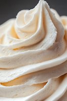 Creamy vanilla frosting swirls with tiny speckles in macro shot showing soft peaks and smooth texture, perfect for bakery and dessert marketing materials.