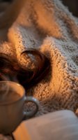 Cozy autumn scene with warm knitted sweater, brown hair curl and steaming coffee mug in golden candlelight creating hygge atmosphere for relaxation.