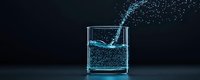 Glowing blue liquid splashing in glass container against dark background creates dynamic motion effect with scattered droplets and luminous water movement.