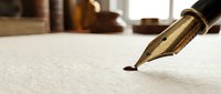 Elegant gold fountain pen nib touching white paper surface in warm lighting, ready for writing letters, documents, or creative work in cozy study setting.