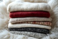 Stacked knit sweaters in neutral and red tones on white fur background, showcasing cozy winter clothing and textile layering for fashion and lifestyle design projects.