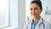 Professional female doctor with stethoscope smiling confidently in modern medical office wearing white coat for healthcare and medicine concepts.