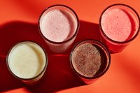 Assortment of colorful smoothies in glasses on vibrant orange background, showcasing healthy breakfast options for detox and nutrition.
