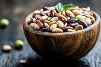 Assorted colorful beans in wooden bowl with fresh basil leaf, showcasing variety of legumes for healthy cooking and plant-based protein source.