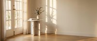 Minimalist interior with marble pedestal table and dried flowers in warm sunlight streaming through French doors creating elegant shadows on wooden floor.